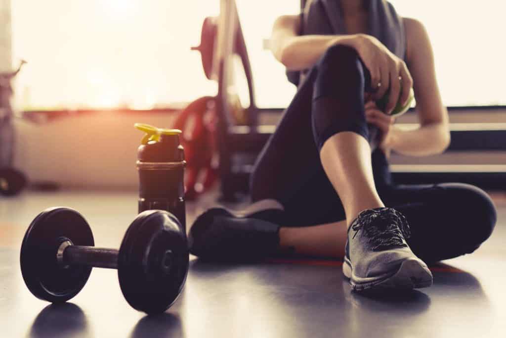 Woman exercise workout in gym fitness breaking relax holding apple fruit after training sport with dumbbell and protein shake bottle healthy lifestyle bodybuilding.