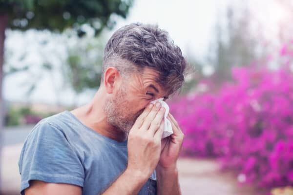 Man sneezing in a tissue outdoors. Pollen allergy, Springtime.