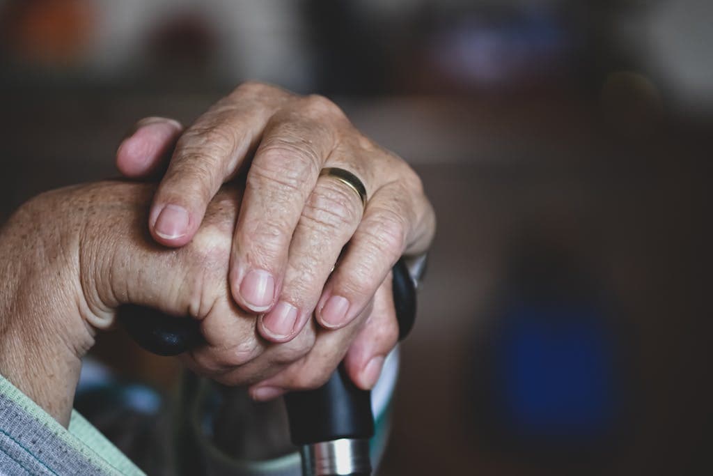 Close-up of senior hands clasped around a cane, highlighting a wedding ring, symbolizing love and support.