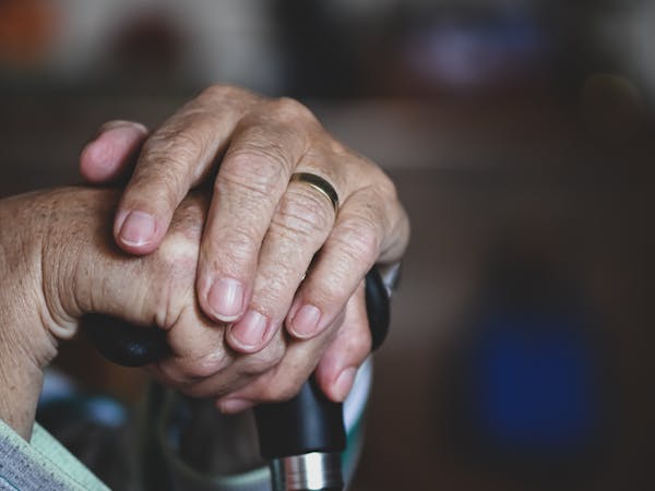 Close-up of senior hands clasped around a cane, highlighting a wedding ring, symbolizing love and support.